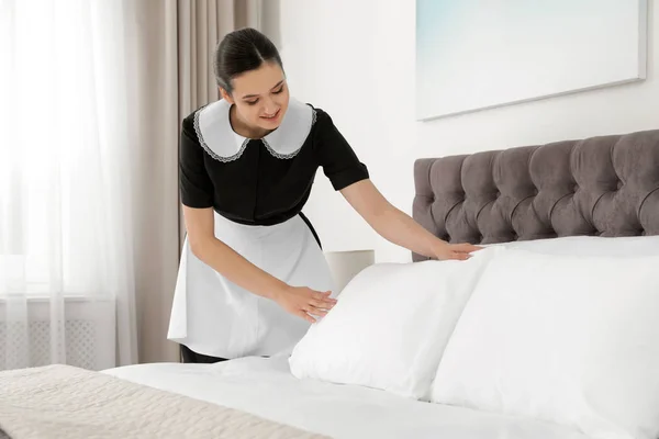 Joven criada haciendo cama en habitación de hotel — Foto de Stock