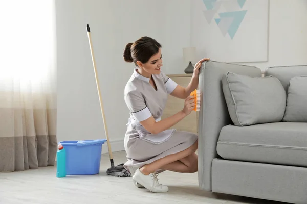 Young maid removing dirt from sofa in hotel room — Stock Photo, Image