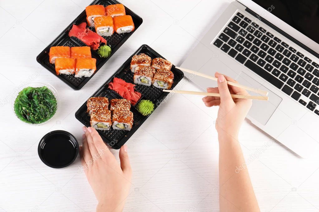 Woman eating tasty sushi rolls at workplace, closeup. Food delivery