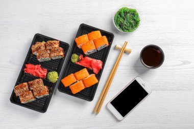 Düz yatıyordu kompozisyon suşi ile rulo, akıllı telefon ve Beyaz ahşap masa üzerinde metin için yer. Food teslim