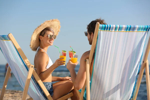 Pareja joven con cócteles en sillas de playa en la costa —  Fotos de Stock