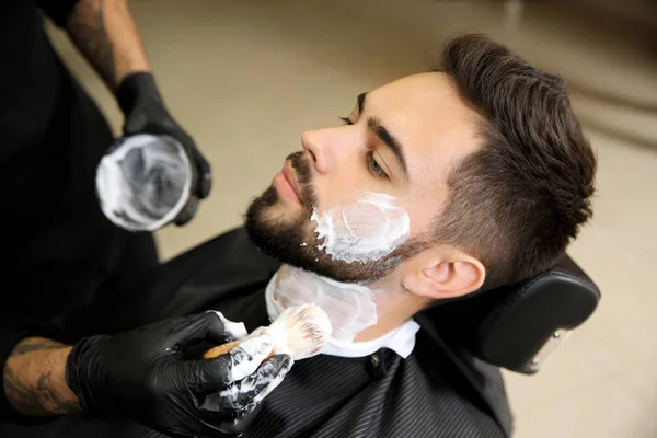 Professional hairdresser applying shaving foam onto client's skin in barbershop — Stock Photo, Image