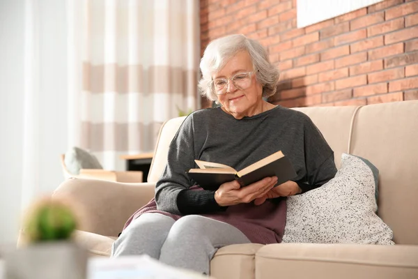 Anciana leyendo libro en sofá en sala de estar —  Fotos de Stock