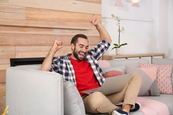 Evde kanepe üzerinde zaferini kutluyor dizüstü bilgisayar ile duygusal genç adam — Stok fotoğraf