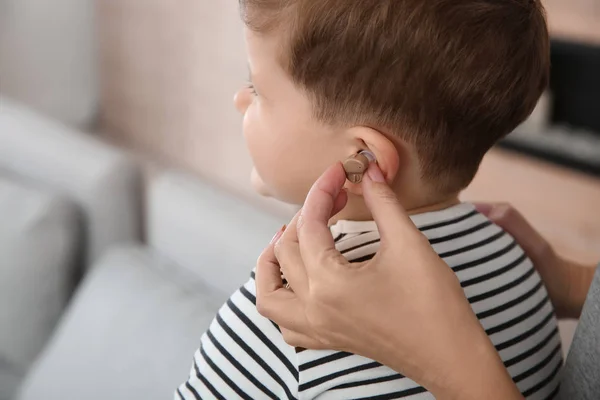 Молода жінка кладе слуховий апарат у вухо маленького сина в приміщенні, крупним планом — стокове фото