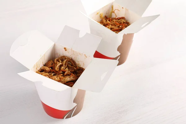 Fideos chinos en cajas de papel sobre mesa de madera blanca. Entrega de alimentos — Foto de Stock