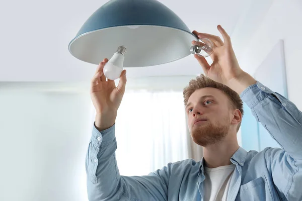 Человек меняет лампочку в подвесной лампе в помещении — стоковое фото
