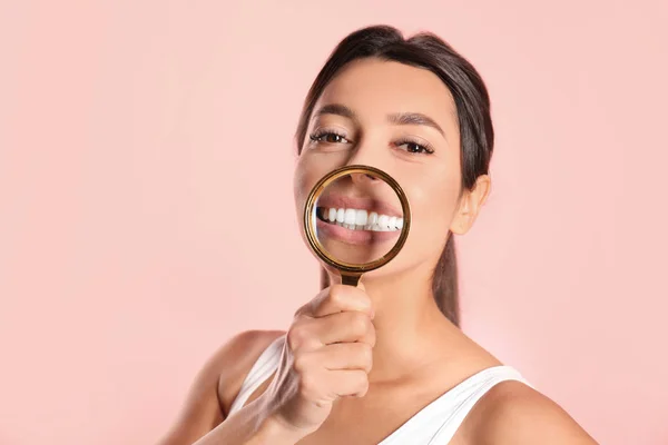 Mujer joven con dientes sanos y lupa sobre fondo de color — Foto de Stock