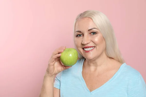 Mujer sonriente con dientes perfectos y manzana verde sobre fondo de color, espacio para texto —  Fotos de Stock