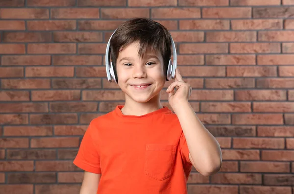 Petit garçon mignon écoutant de la musique avec des écouteurs contre un mur de briques — Photo