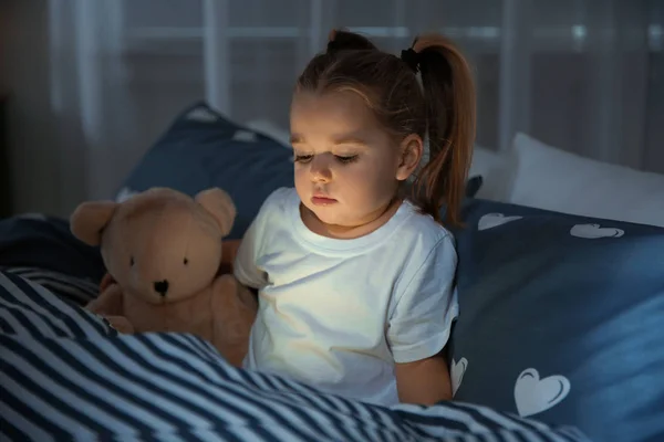 Krásná holčička s miniaplikace a hračku do postele v noci. Před spaním plán — Stock fotografie