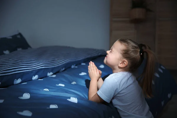 Little girl saying bedtime prayer near bed in room at night — Stock Photo, Image