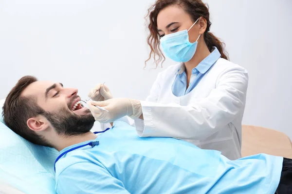 Zahnarzt untersucht Zähne des jungen Mannes mit Spiegel und Sonde im Krankenhaus — Stockfoto