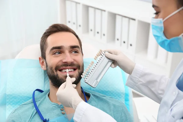 Dentista combinando cor dos dentes do jovem com paleta no escritório — Fotografia de Stock
