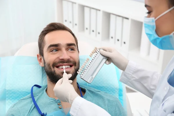 Zahnarzt passt Zahnfarbe des jungen Mannes mit Palette im Büro an — Stockfoto