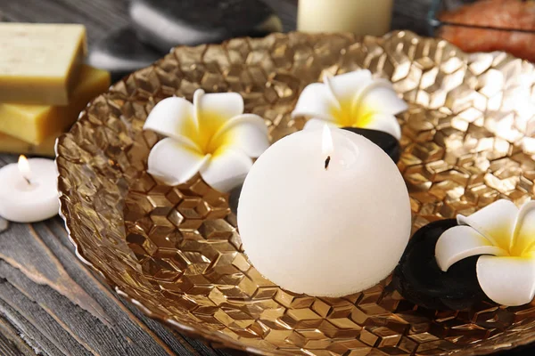 Candle, spa stones and flowers in plate with water on table