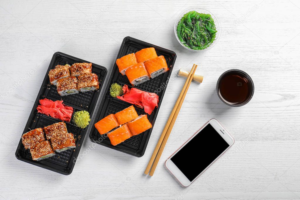 Flat lay composition with sushi rolls, smartphone and space for text on white wooden table. Food delivery