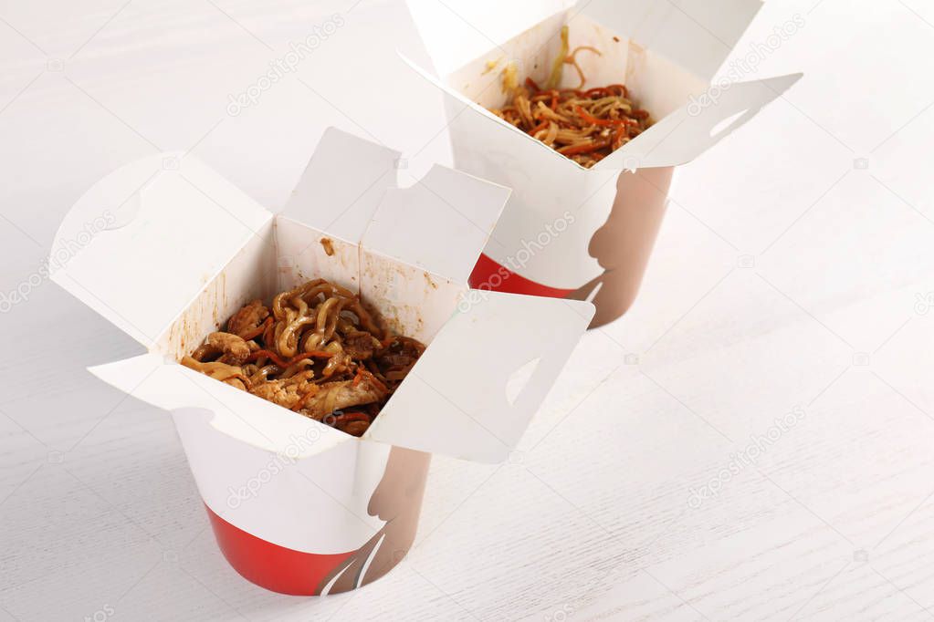 Chinese noodles in paper boxes on white wooden table. Food delivery