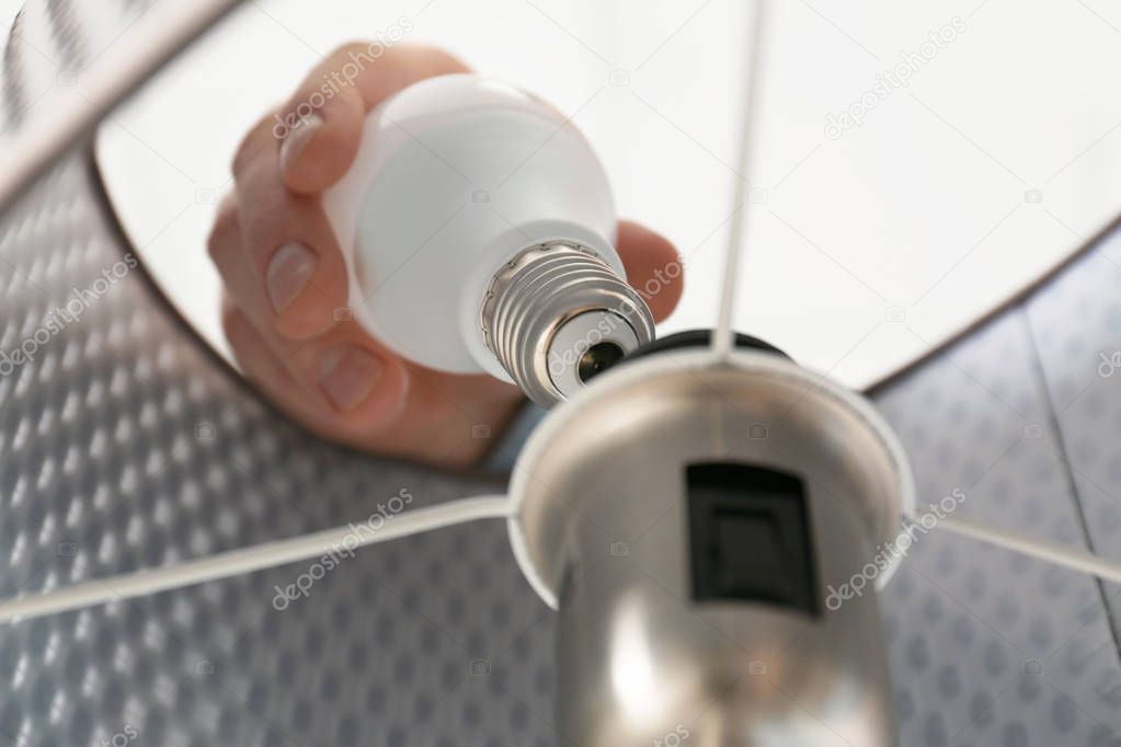 Man changing light bulb in lamp, closeup. Low angle view