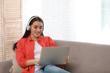 Genç kadın kanepe oturma odasında üstünde laptop ve kulaklık ile