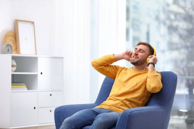 Evde koltukta oturan kulaklıklar ile genç adam