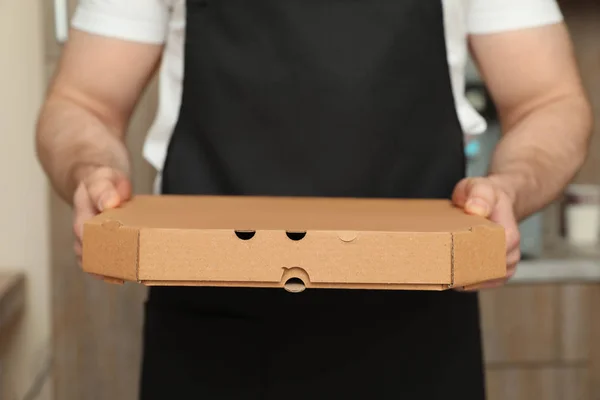 Waiter in apron with pizza box indoors, closeup. Food delivery service — Stock Photo, Image