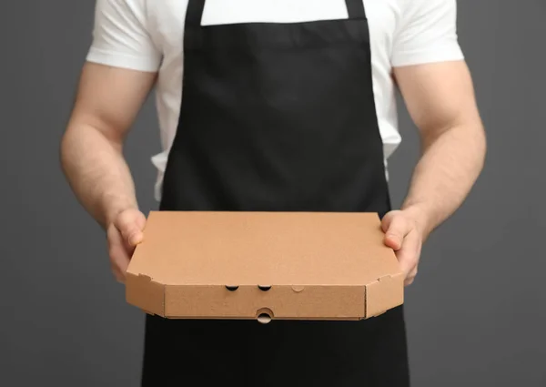 Ober in schort met de doos van de pizza op een grijze achtergrond, close-up. Levering foodservice — Stockfoto