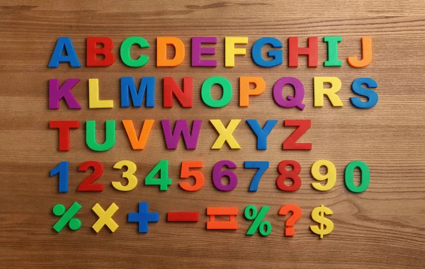 Plast magnetiska bokstäver, siffror och matematiska symboler på trä bakgrund, ovanifrån — Stockfoto