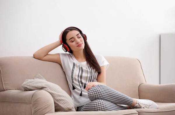 Mladá žena ve sluchátkách, poslech hudby na gauči doma — Stock fotografie