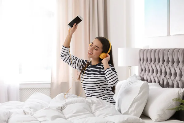 带着耳机和移动设备在床上欣赏音乐的年轻女子 — 图库照片