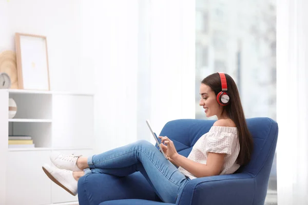 Mujer joven con auriculares y tableta sentada en sillón en casa — Foto de Stock