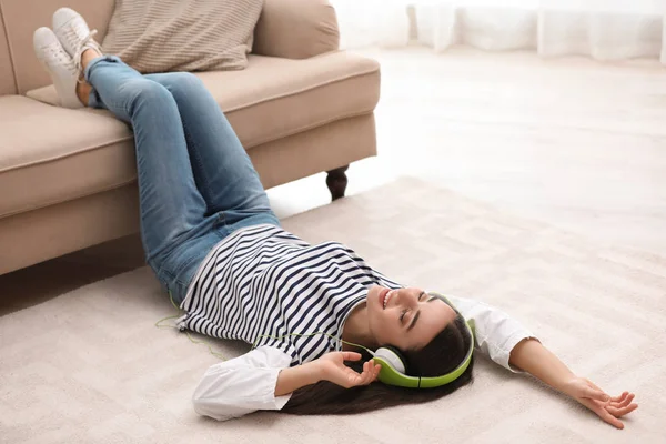 Mladá žena s sluchátka poslouchat hudbu na podlahu v obývacím pokoji — Stock fotografie