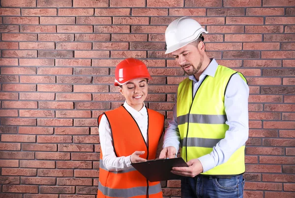 Ingenieros industriales en uniformes con portapapeles sobre fondo de pared de ladrillo. Equipo de seguridad — Foto de Stock