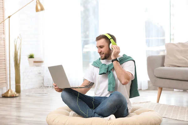 Jeune homme avec écouteurs et ordinateur portable assis sur le sol dans le salon — Photo
