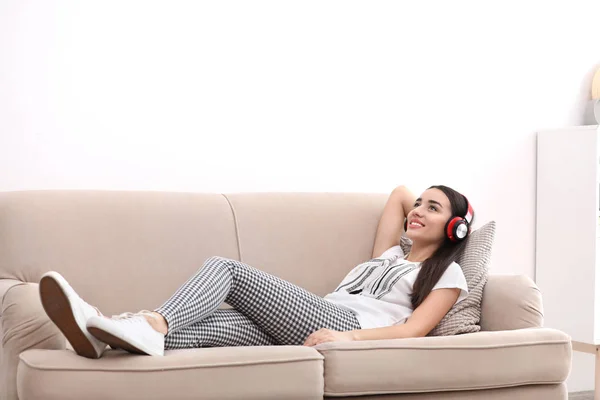 Jovem mulher em fones de ouvido desfrutando de música no sofá em casa — Fotografia de Stock