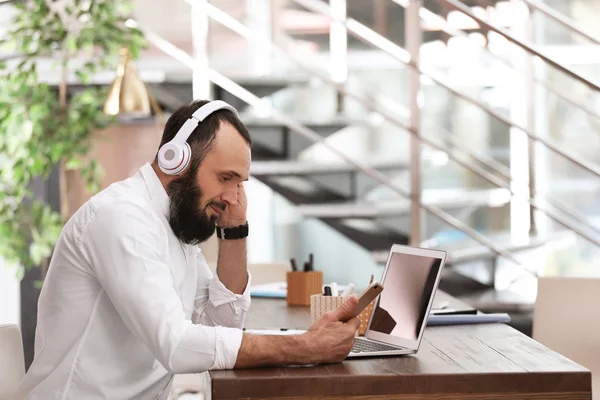 Hombre maduro con auriculares y portátil trabajando en la oficina en casa —  Fotos de Stock