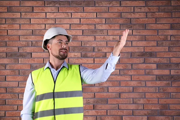 Ingeniero industrial masculino en uniforme sobre fondo de pared de ladrillo, espacio para texto. Equipo de seguridad —  Fotos de Stock