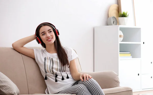 Jovem mulher em fones de ouvido desfrutando de música no sofá em casa — Fotografia de Stock