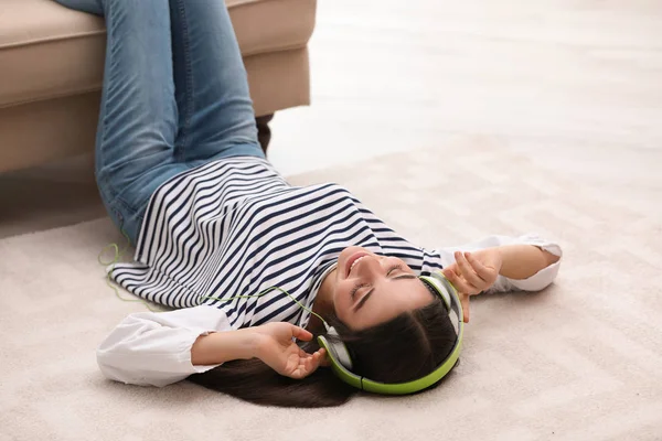 Jonge vrouw met hoofdtelefoon luisteren naar muziek op de vloer in de woonkamer — Stockfoto