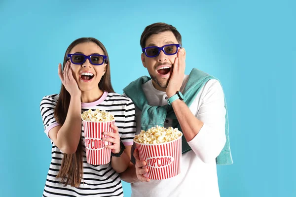 Emotional couple with 3D glasses and tasty popcorn on color background
