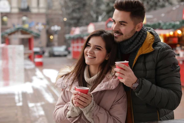 Young couple with cups of mulled wine at winter fair. Space for text — Stock Photo, Image