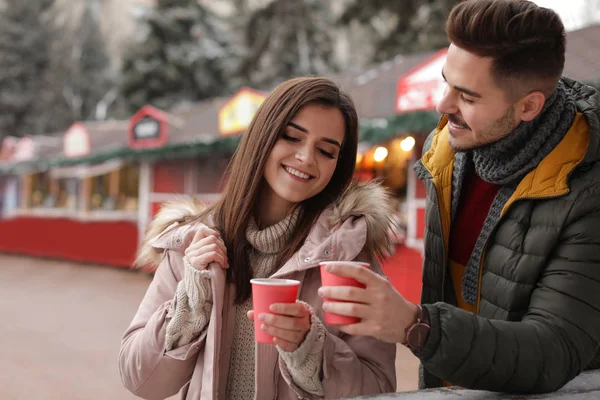 Young couple with cups of mulled wine at winter fair. Space for text — Stock Photo, Image