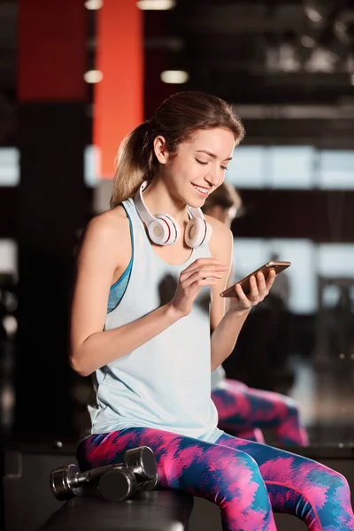 Jonge vrouw met hoofdtelefoons en mobiele apparaat op sportschool — Stockfoto