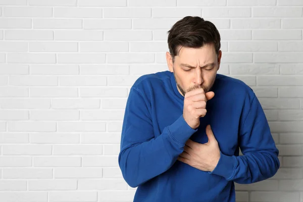 Hombre que sufre de tos cerca de la pared de ladrillo. Espacio para texto —  Fotos de Stock