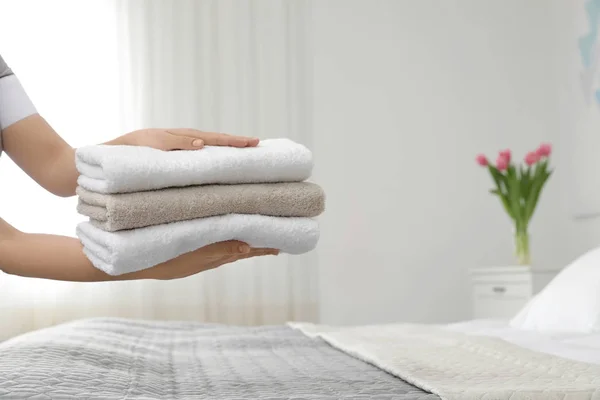 Joven criada sosteniendo una pila de toallas frescas en la habitación del hotel, primer plano —  Fotos de Stock