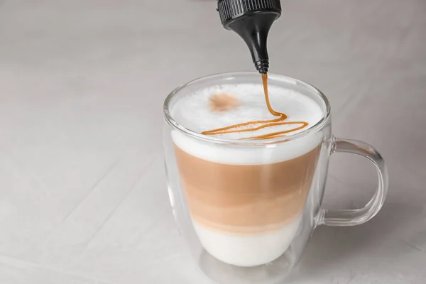 Adding caramel topping to latte macchiato on table — Stock Photo, Image