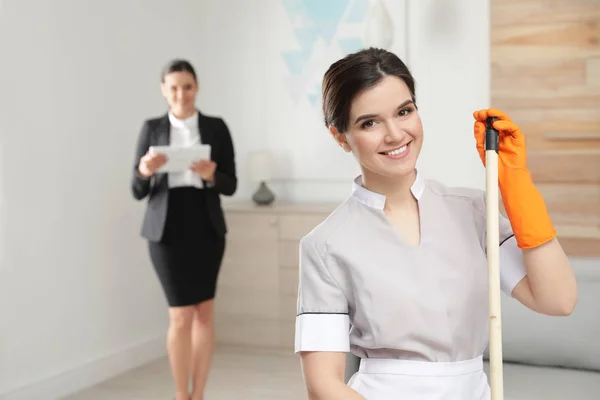 Jovem empregada doméstica com esfregona e gerente de limpeza no quarto de hotel — Fotografia de Stock