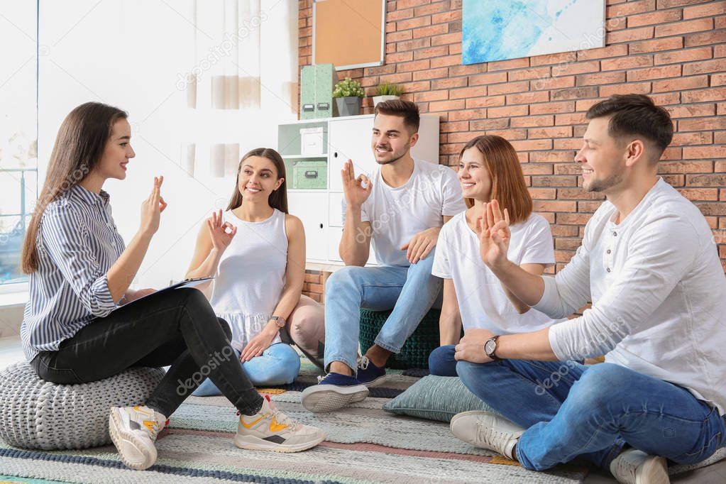 Group of young people learning sign language with teacher indoors