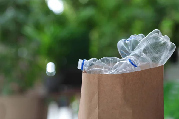 Used plastic bottles in paper bag on blurred background, space for text. Recycling problem — Stock Photo, Image