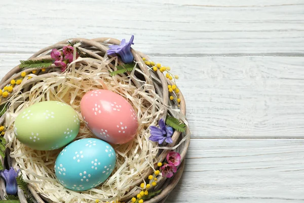 Nid en osier avec œufs de Pâques peints et fleurs sur table en bois, vue sur le dessus. Espace pour le texte — Photo